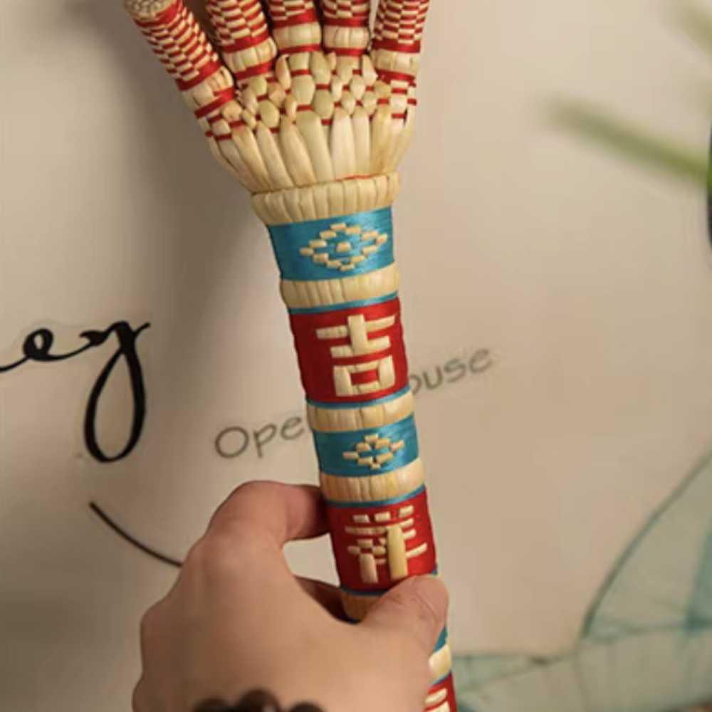 a hand gripping the sorghum hand's corded handle, close detail on the woven lucky character, uggaz
