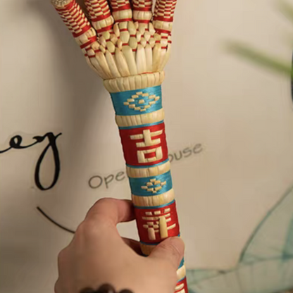 a hand gripping the sorghum hand's corded handle, close detail on the woven lucky character, uggaz